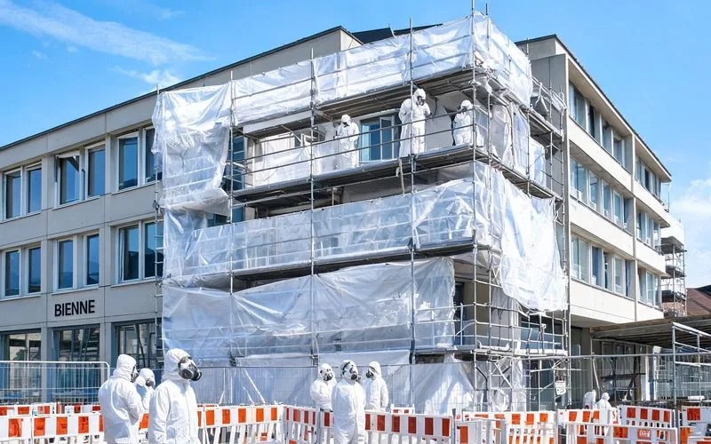 Opérateurs en combinaison blanche sur un chantier de désamiantage confiné devant un immeuble à Bienne